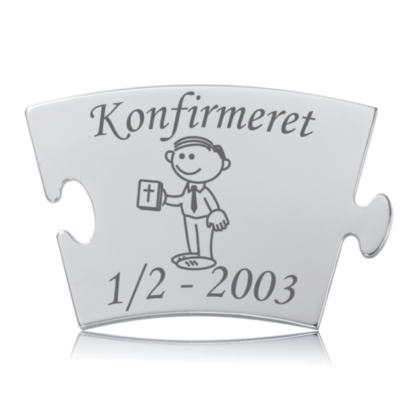 Konfirmeret Dreng Memozz Classic Brik Blank, rektangulær puslespilsformet Memozz Classic brik i håndpoleret rustfrit stål, designet til konfirmationsmilepælen. Brikken, er graveret med ordet "Konfirmeret" i en elegant skrifttype samt en charmerende illustration af en konfirmationsklar dreng, der holder en bog med et kors på. Graveringen fremstår i mørkegrå nuancer mod den skinnende stål overflade, hvilket understreger den høje detaljegrad og håndværksmæssige kvalitet. Billedet taget med hvid baggrund fremhæver brikkens skinnende finish og rene linjer.