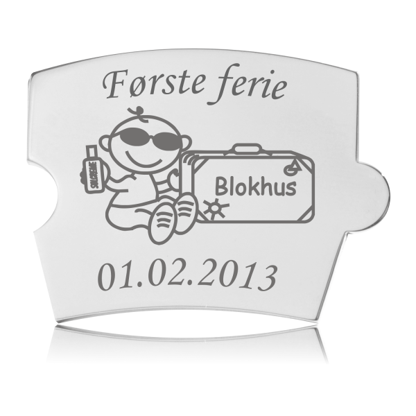 Memozz Spin brik i skinnende rustfrit stål med gravering af teksten "Første ferie", en tegnet figur med solbriller og solcreme, og en kuffert med teksten "Blokhus".