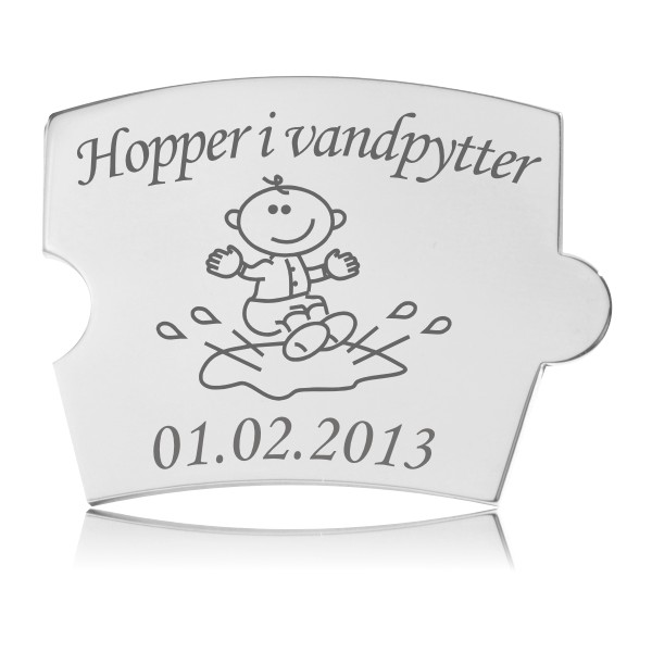 Memozz Spin brik i håndpoleret rustfristål med gravering af et barn der hopper i vandpytter, med vandstænk omkring barnet.