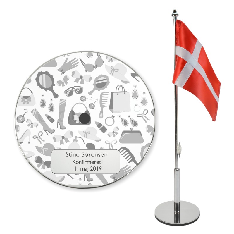 Konfirmationsflag med gravering på rund fod med motiv af pige ting som taske, sko og smykker, ved siden af Dannebrogsflag på stage.