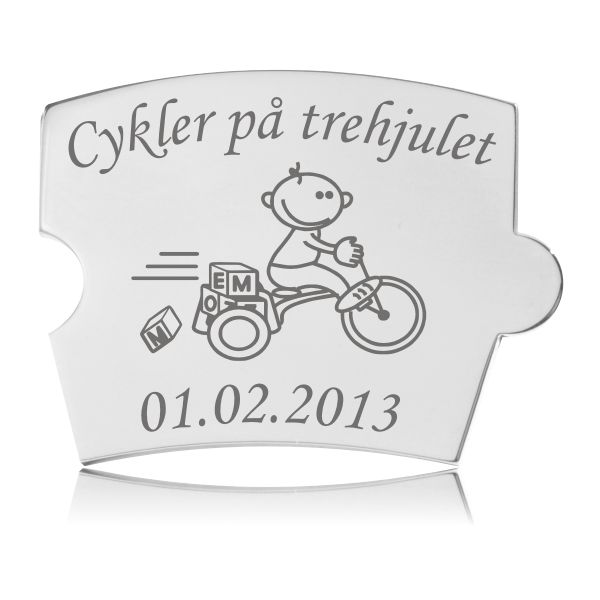 Blank, sølvfarvet Memozz Spin mindebrik med illustration af barn på trehjulet cykel og tekst "Cykler på trehjulet"