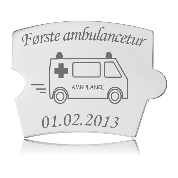 Memozz Spin brik i blankpoleret rustfrit stål med gravering af en ambulance og teksten "Første ambulancetur"
