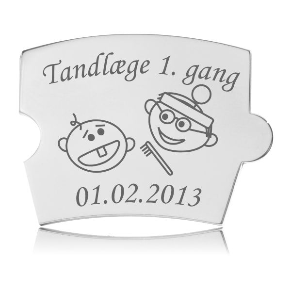 Memozz Spin brik i poleret rustfrit stål med gravering af en baby med én tand og en tandlæge med tandbørste, tekst "Tandlæge 1. gang" og plads til dato.