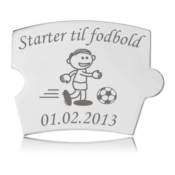 Memozz Spin brik i stål med gravering af dreng der starter til fodbold, vist på hvid baggrund.