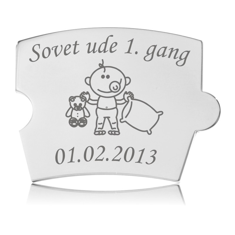 Memozz Spin brik i håndpoleret rustfrit stål med teksten "Sovet ude 1. gang" og et stregtegnet barn med bamse og pude