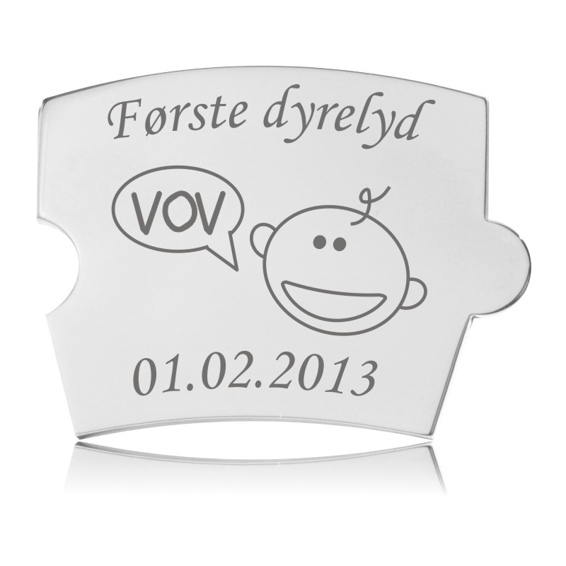 Memozz Spin brik i poleret stål med gravering af 'Første dyrelyd' og en tegning af et babyansigt, der siger 'VOV'.