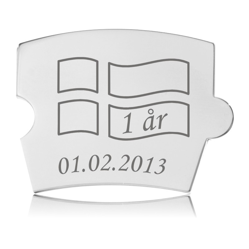 Sølvfarvet Memozz Spin brik i bølget flag-form med graveret design til fødselsdag. Teksten "1 år" er skrevet. Den er fremstillet i håndpoleret rustfrit stål.