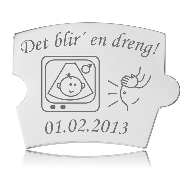 Memozz Spin brik i håndpoleret rustfrit stål med teksten "Det blir' en dreng!", sonogram-ikon og hænder på gravid mave.