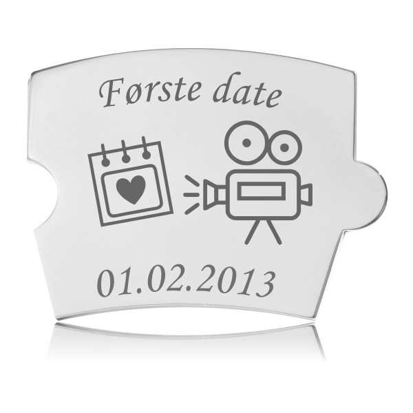 Memozz Spin brik i håndpoleret rustfrit stål med teksten "Første date", et kalenderikon med hjerte og et filmkamera, graveret i mørkegrå.