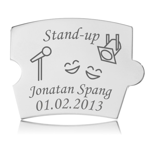 Memozz Spin Stand-up brik i poleret rustfrit stål med gravering af mikrofon, spotlys og glade smileys. Mindesjov oplevelse.