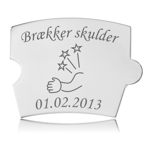 Memozz Spin brik i håndpoleret rustfrit stål med teksten "Brækker skulder" og en illustration af en arm med stjerner og pil, der symboliserer et uheld, graveret i mørkegrå.