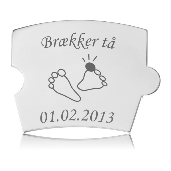Memozz Spin Brik Brækker Tå i rustfrit stål Rektangulær Memozz Spin brik i håndpoleret rustfrit stål med gravering af teksten "Brækker tå", to små fødder med en rød prik på en tå, samt datoen "01.02.2013".