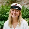 Glad student med studenterhue smiler i grønne omgivelser med naturligt lys